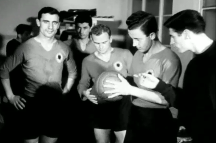 Qemal Vogli (dressed in black in the far right) pointing at the ball in the dressing room of the Albanian National Team on 7 January 1953 prior to the away friendly match against Poland; a frame from a video chronicle retrived from digitalised National Polish Archive.